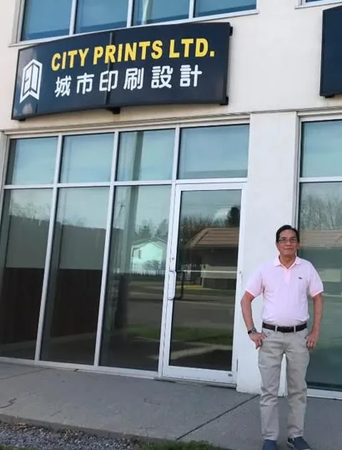Tommy standing outside City Prints beside its bilingual sign.